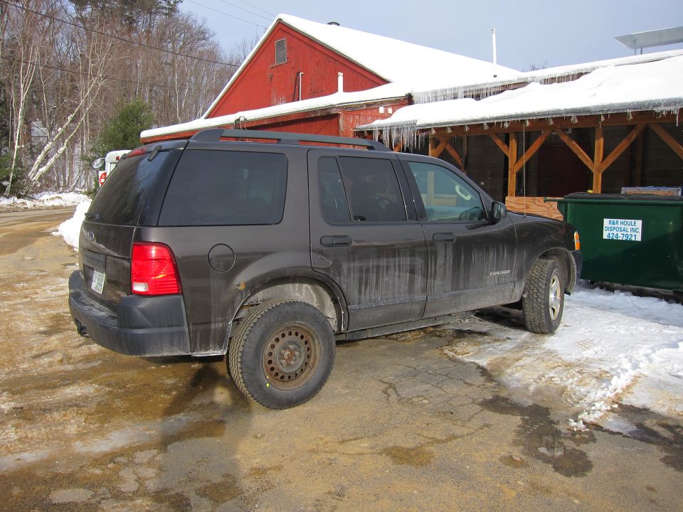 Dark gray Ford Explorer parked on wet ground with snow, red barn in background