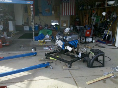1996 Ford Bronco - An engine is mounted on a stand in a garage, surrounded by various tools and automotive equipment.