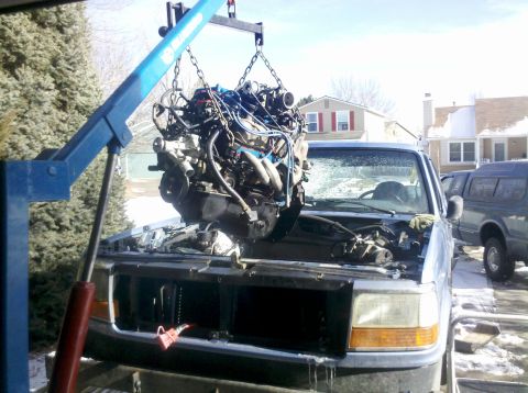 1996 Ford Bronco - An engine is being removed from a truck using an engine hoist in a residential driveway.