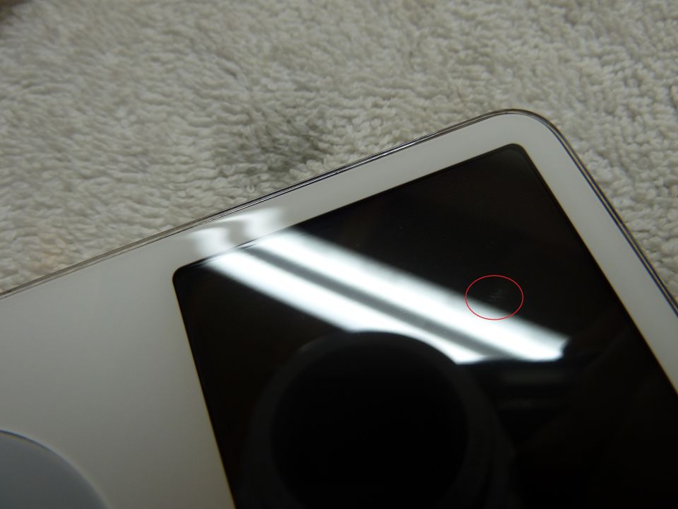 White electronic device with a black screen showing a small imperfection circled in red