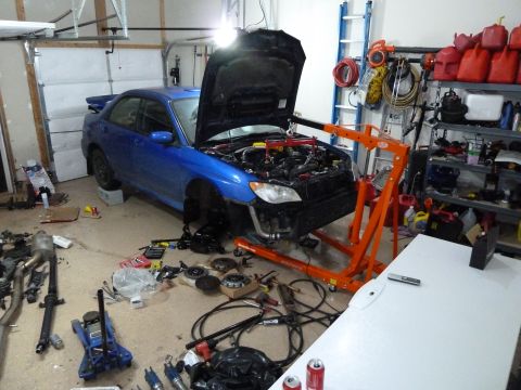 2007 Subaru Impreza - A blue 2007 Subaru Impreza is in a garage with its hood open and engine removed, surrounded by various car parts and tools.