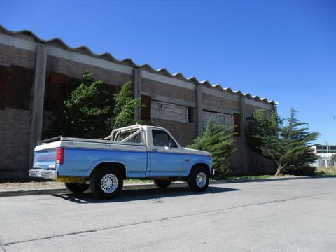 1983 Ford F-100 - A light blue and white pickup truck is parked on the side of a road next to a building.