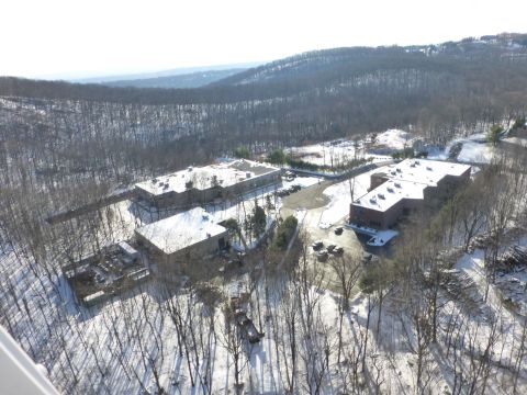 1959 Kenworth W900A - Several industrial buildings are visible from above, set against a backdrop of snow-covered trees and hills.