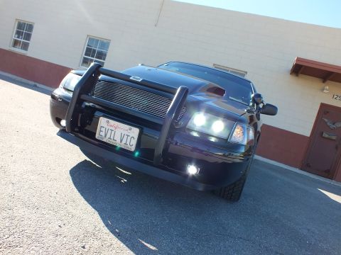 2003 Ford Crown Victoria - Head-on low shot of a black sedan, illuminated headlights, brush guard and California plate reading EVIL VIC.