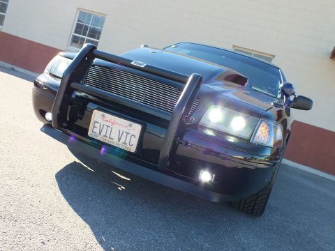 2003 Ford Crown Victoria - Close front view of a black sedan with billet grille, brush guard and lit headlights above an EVIL VIC plate.