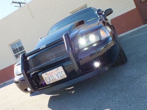 2003 Ford Crown Victoria - Tilted low shot of a black sedan front, projector lights on, brush guard and California EVIL VIC plate.