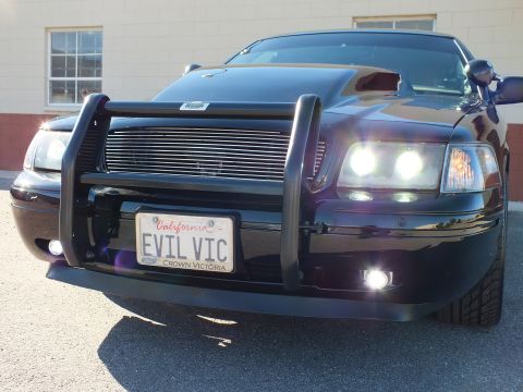 2003 Ford Crown Victoria - Front detail of a black sedan: billet grille, tubular guard, fog lamps and California plate frame reading Crown Victoria.