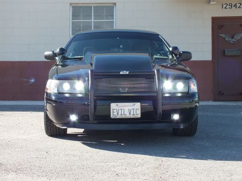 2003 Ford Crown Victoria - Front of a black sedan with raised hood scoop, billet grille, lit projector lights and EVIL VIC California plate.