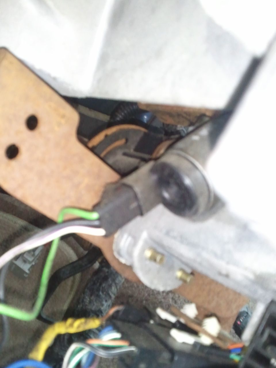 Close-up of a wiring harness connector with green, white, and purple wires, attached to a metal bracket under a dashboard