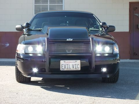 2003 Ford Crown Victoria - Black sedan photographed straight on, headlights and fog lights on, EVIL VIC plate with Crown Victoria frame.