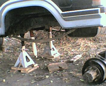 1984 Ford Bronco - The rear axle assembly of a vehicle is supported by jack stands, with suspension components visible.