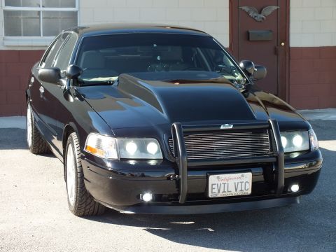 2003 Ford Crown Victoria - Front right angle of a black sedan with tubular guard, billet grille and illuminated projector headlights.