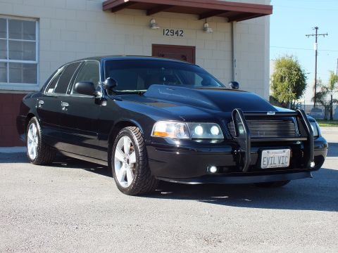 2003 Ford Crown Victoria - Black sedan shown from front left, lowered on polished five-spoke wheels with grille guard and EVIL VIC plate.