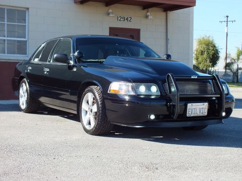 2003 Ford Crown Victoria - Front-left view of a lowered black sedan with brush guard, billet grille and lit projector headlights.