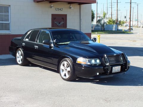 2003 Ford Crown Victoria - Black sedan from front right showing brush guard, billet grille and California EVIL VIC plate near building 12942.