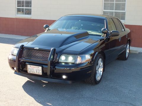 2003 Ford Crown Victoria - Front-left view of a black sedan, projector headlights and fog lamps on, brush guard and EVIL VIC California plate.