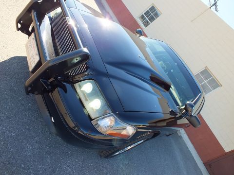 2003 Ford Crown Victoria - Angled detail of a black sedan's front, dual projector headlight, side mirror and tubular grille guard.