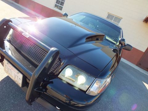 2003 Ford Crown Victoria - Dramatic angled shot of a black sedan front: billet grille, brush guard, lit projector lights and EVIL VIC plate.