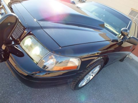 2003 Ford Crown Victoria - Close detail of a black Crown Victoria sedan's front fender, headlight, side mirror and alloy wheel under bright sun