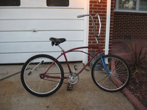 1994 Ford Bronco - A red cruiser bicycle with a black seat and handlebars is parked outside a brick house with a white garage door.