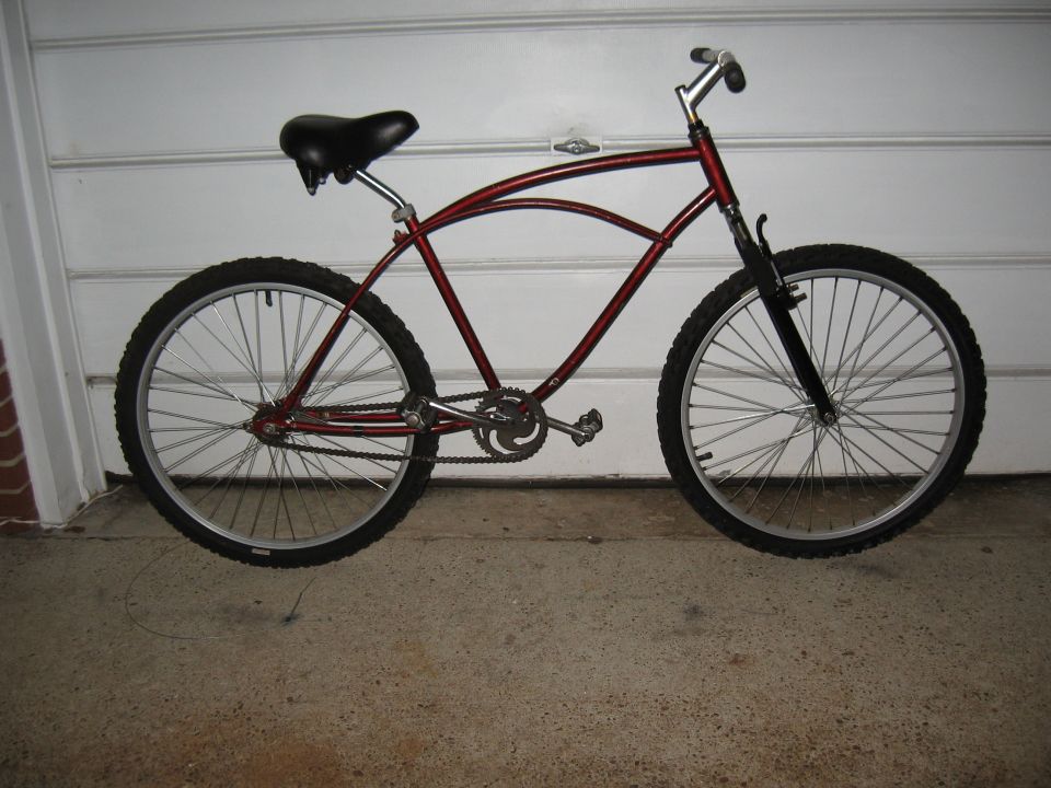 Red cruiser bicycle with black seat and tires, parked indoors