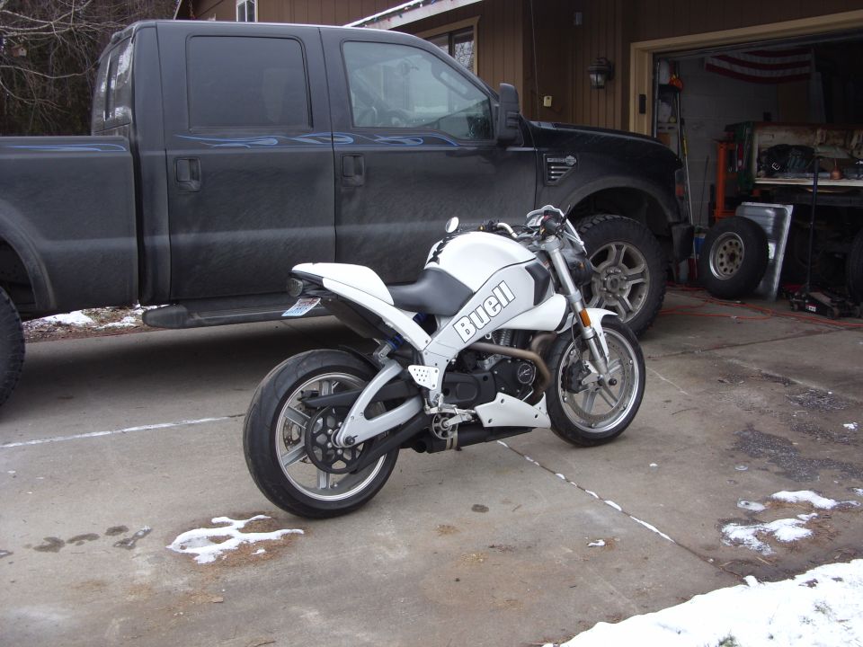 White Buell motorcycle parked in front of a black pickup truck