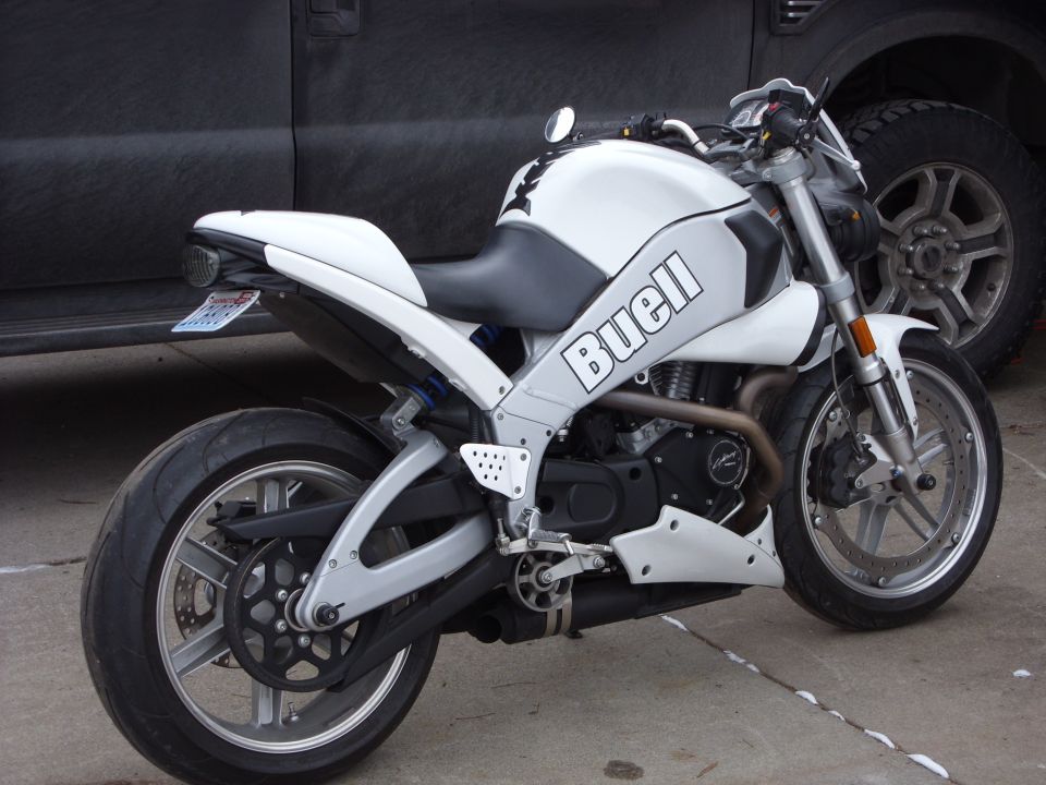 White Buell motorcycle side view parked next to a dark truck