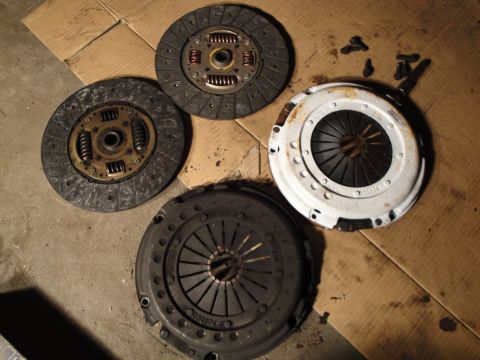 1992 Ford Taurus - A collection of clutch assemblies and loose bolts are laid out on a surface of cardboard and concrete.