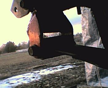 1984 Ford Bronco - A close-up view of a rusty metal component, likely part of a vehicle's suspension or axle system, against a blurred outdoor backdrop.