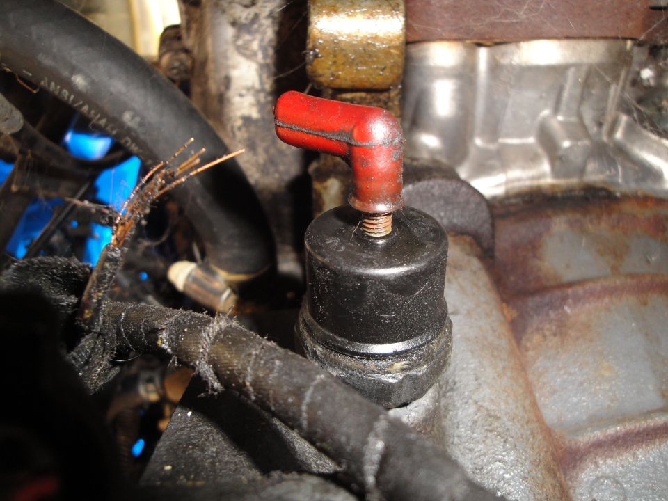 Engine part with red spark plug wire boot and frayed black wire loom