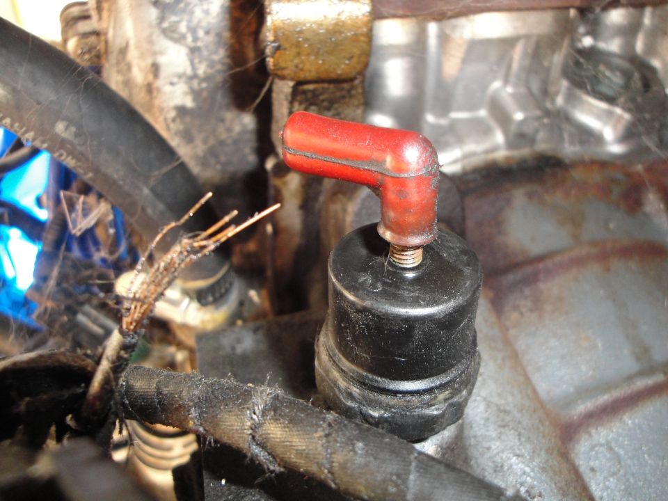 Close-up of a black engine sensor with a red angled cap and frayed wires
