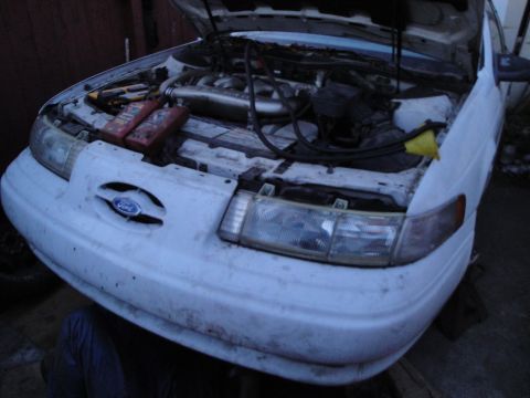 1992 Ford Taurus - Front view of a white 1992 Ford Taurus with its hood open, revealing the engine and two red fluid containers.