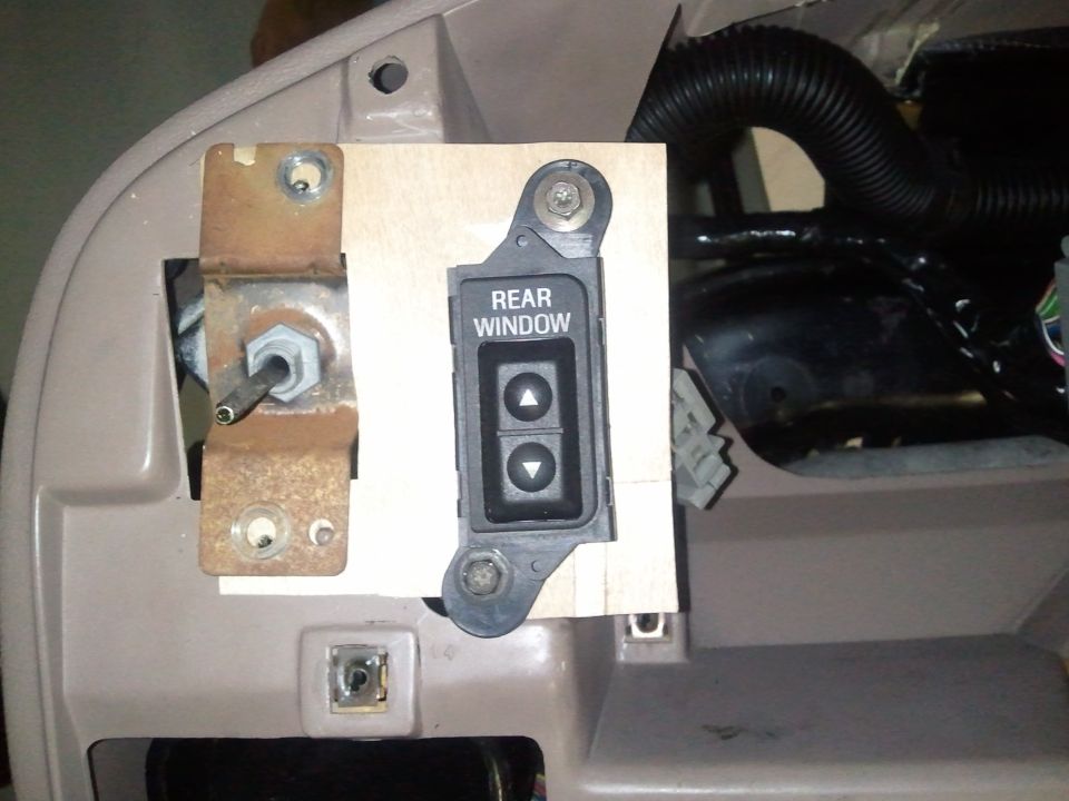 Rear window switch assembly mounted on a wooden bracket, showing wiring and interior dash components