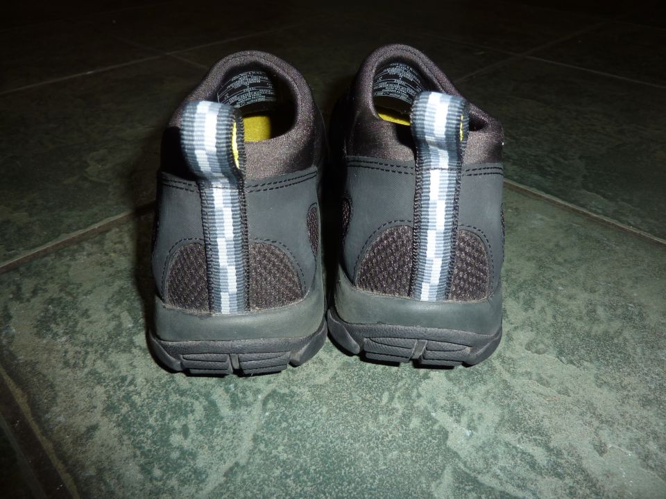 Back view of a pair of dark gray shoes with yellow lining and reflective heel tabs