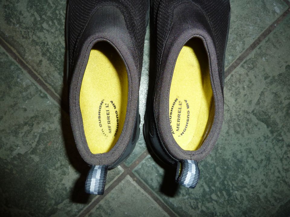 Close-up of the insoles of two dark slip-on shoes, showing "MERRELL AIR CUSHION" text