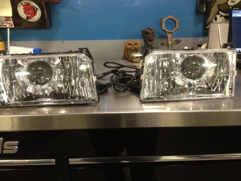 1995 Ford Bronco - A pair of aftermarket projector headlights are displayed on a workbench, ready for installation.
