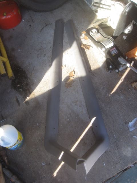 1993 Ford Bronco - Two gray plastic trim pieces are laid out on a concrete surface with a metal bracket attached to one.