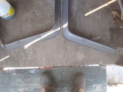 1993 Ford Bronco - Two gray plastic trim pieces are laid out on a concrete surface, possibly for sale or repair.