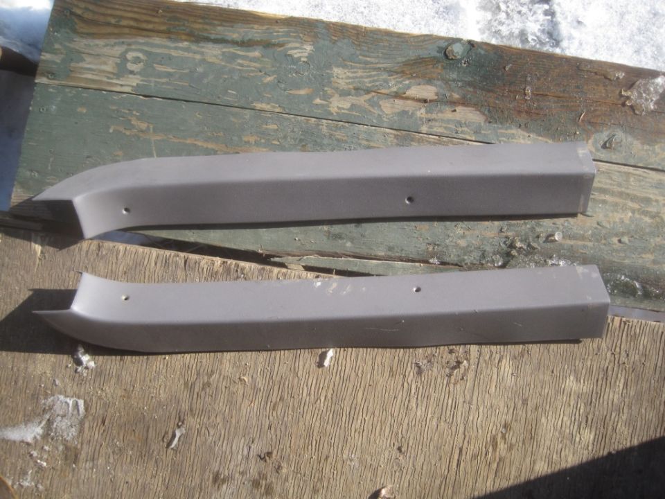 Two gray plastic door trim pieces with screw holes, resting on weathered wood