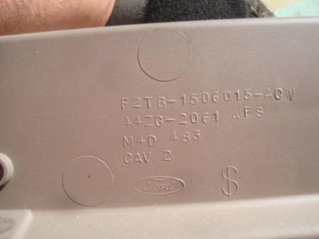 1993 Ford Bronco - A tan plastic automotive part displays embossed text and a Ford logo, indicating it is a component from a Ford vehicle.