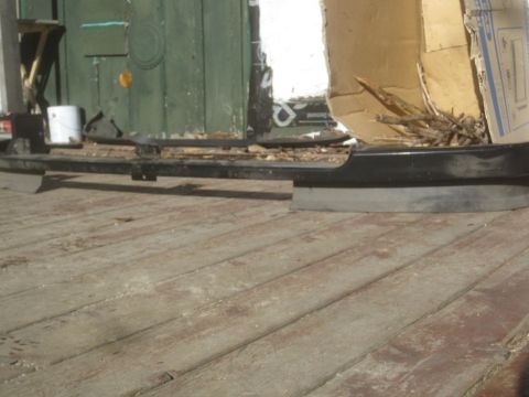 1993 Ford Bronco - Black bumper part resting on a wooden deck, with a green door and cardboard in the background.