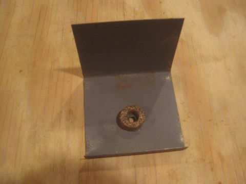 1993 Ford Bronco - Metal bracket with a nut, likely a vehicle part, shown on a wooden background.