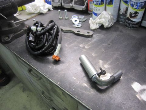 2008 Jeep Wrangler - A close-up view of a wiring harness and a bent exhaust pipe, along with various tools and spray cans, laid out on a workbench.
