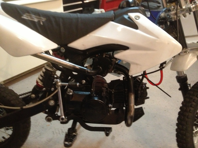 Dirt bike with white body panels and black seat. Engine and suspension visible