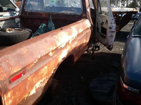 1994 Ford Bronco - This heavily rusted pickup truck is in a junkyard setting with other vehicles visible.