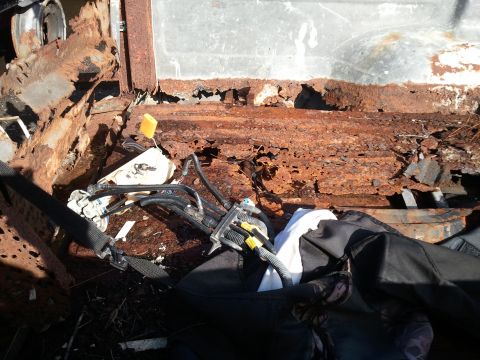 1994 Ford Bronco - The interior of a vehicle shows extensive rust damage and exposed mechanical components.