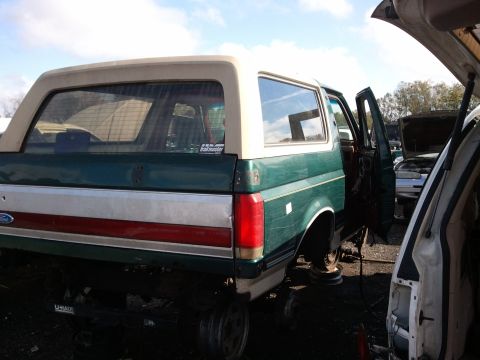 1994 Ford Bronco - This green Ford Bronco is in a junkyard with its doors open and other vehicles nearby.