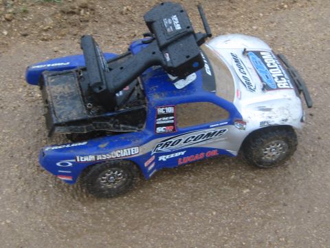 1996 Ford Bronco - RC truck with remote control sits on wet ground, covered in dirt and mud.
