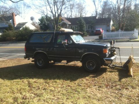 1989 Ford Bronco - This black Ford Bronco is equipped with a snow plow and parked on a grassy area.