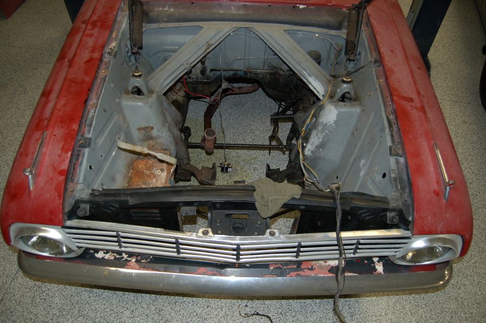 Red vintage Ford with hood removed showing empty, stripped engine bay during restoration in a shop